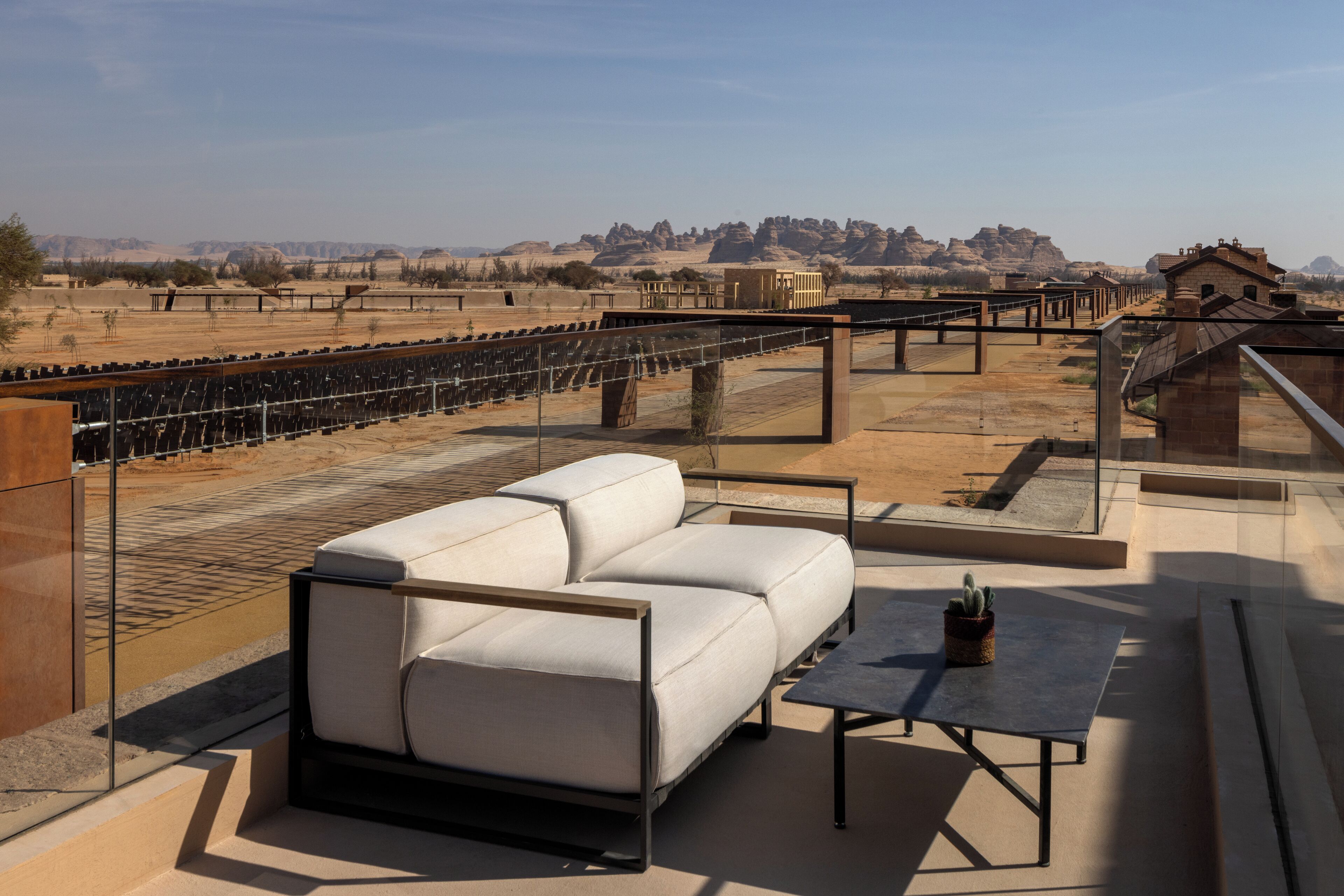 A rooftop terrace with a white sofa and a table, overlooking a desert landscape with distant mountains.