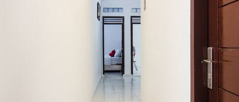 A narrow hallway with a door on the right and a bed with a red pillow in the distance.