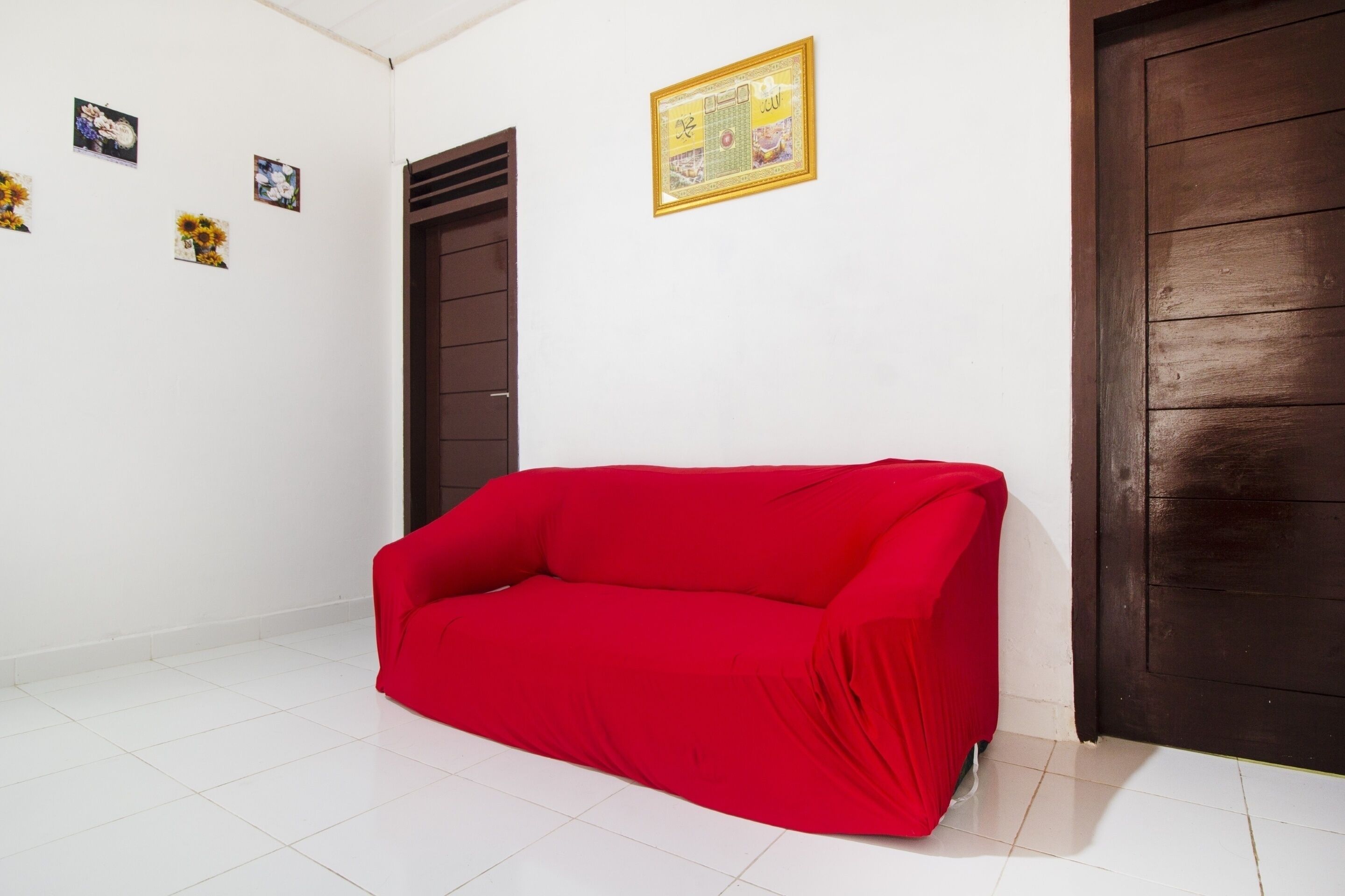 A room with a red sofa, white tiled floor, a brown door, and a framed picture on the wall.