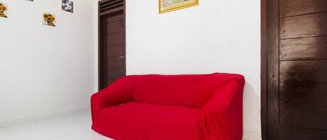 A room with a red sofa, white tiled floor, a brown door, and a framed picture on the wall.