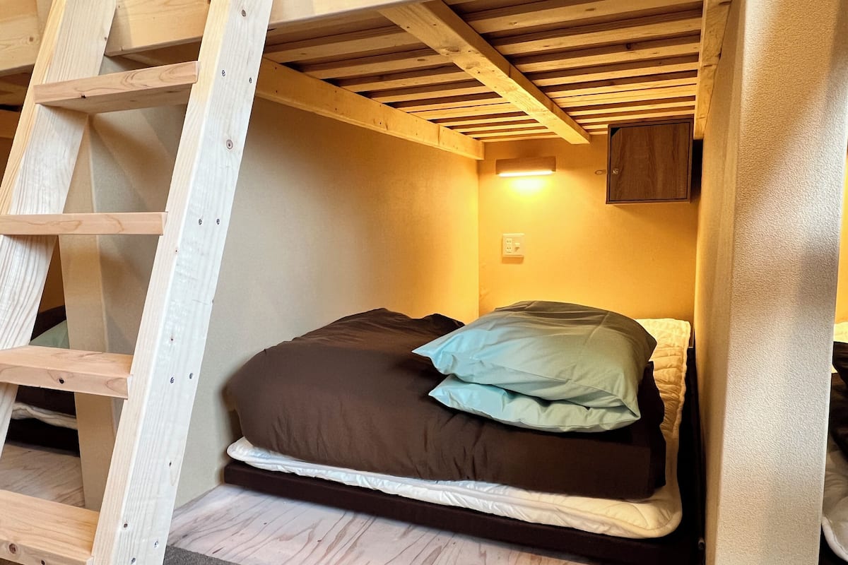 Ein Stockbett mit einer Leiter, ein Einzelbett mit Kissen und ein kleines Schränkchen unter einer geneigten Decke.