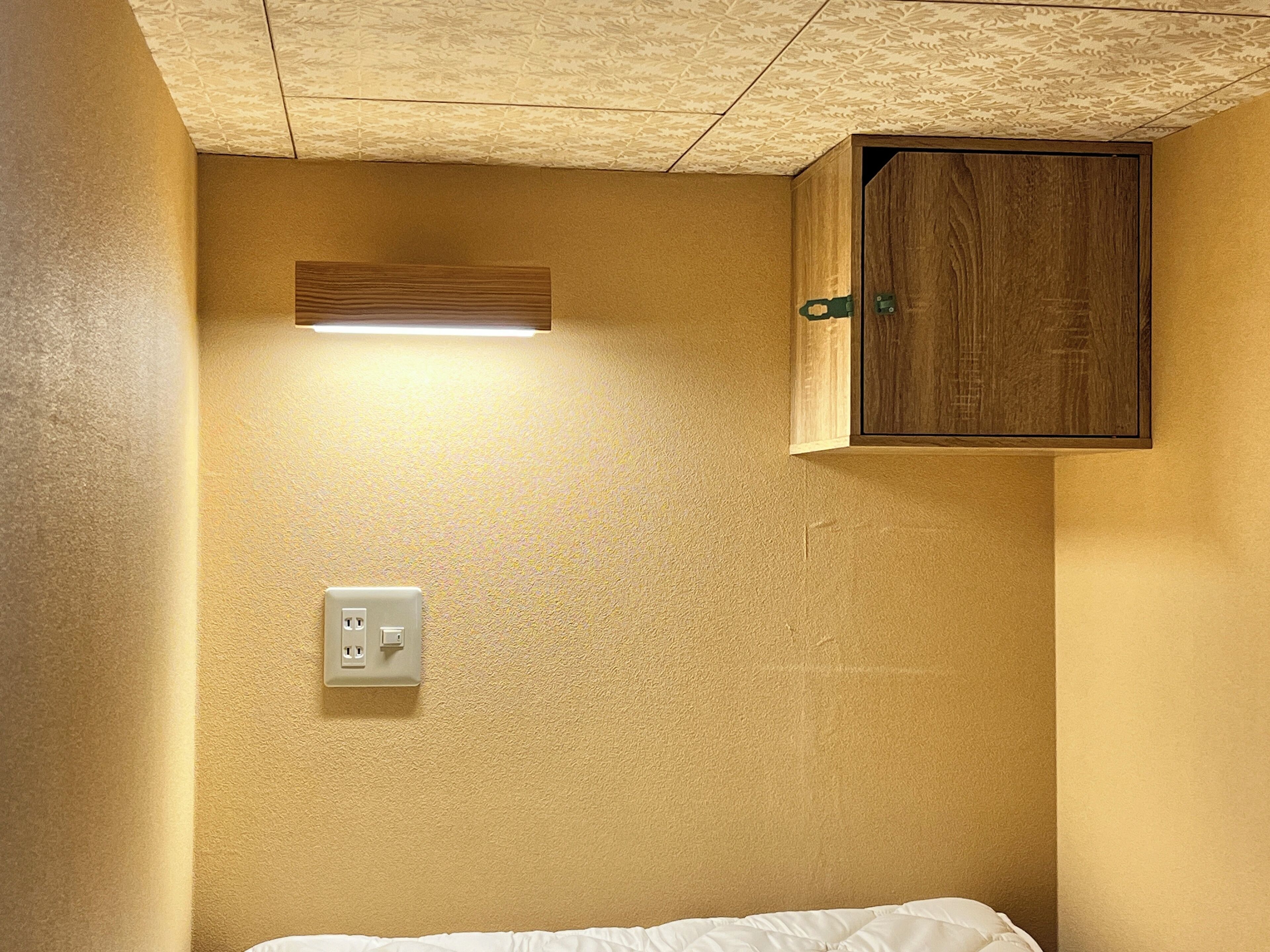 Una habitación con una cama, un armario de madera, una lámpara y un enchufe en la pared.