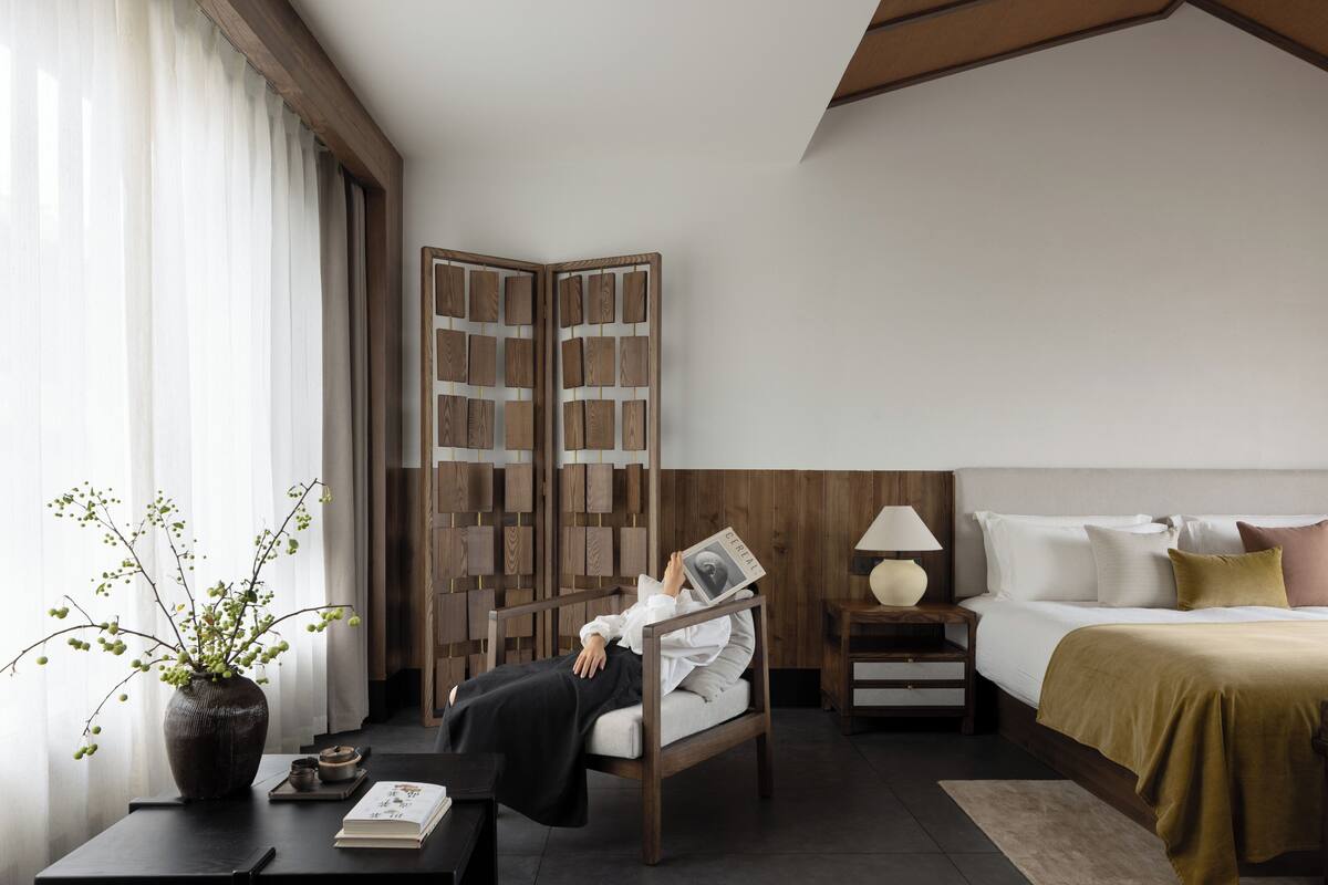 Ein modernes Hotelzimmer mit Bett, Nachttisch, Lampe und einem dekorativen Holzschirm.