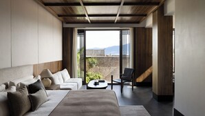 A modern bedroom with a large bed, a sofa, a coffee table, and a chair. There is a view of a traditional building and mountains through the window. - LA MAISON . View Resort (Lijiang)