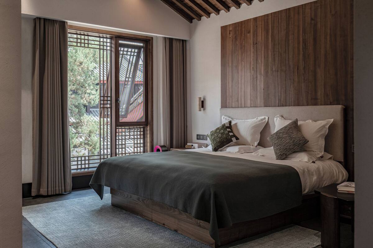 Ein modernes Schlafzimmer mit einem großen Bett, einem Holzkopfende und Blick durch ein Fenster mit Vorhängen.