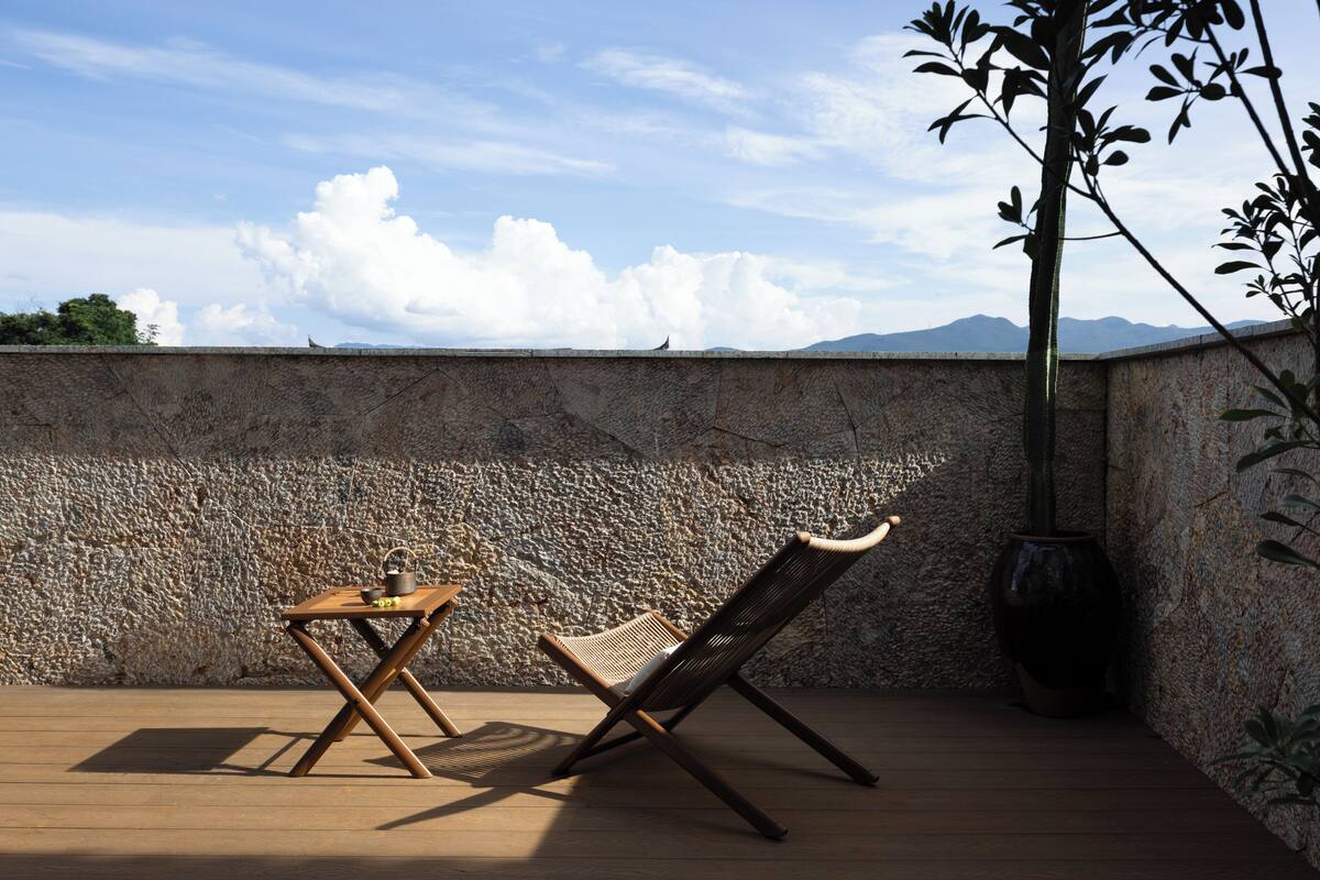 Eine Holzterrasse mit Tisch und Stuhl, eine Steinmauer und ein Blumentopf.