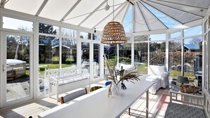 Une véranda avec une table blanche, des chaises et un luminaire suspendu.