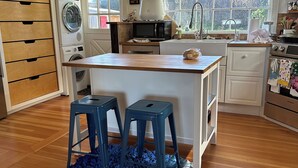 A kitchen with wooden cabinets, a built-in washing machine, a microwave, and a sink. There are two stools and a blue rug on the floor.