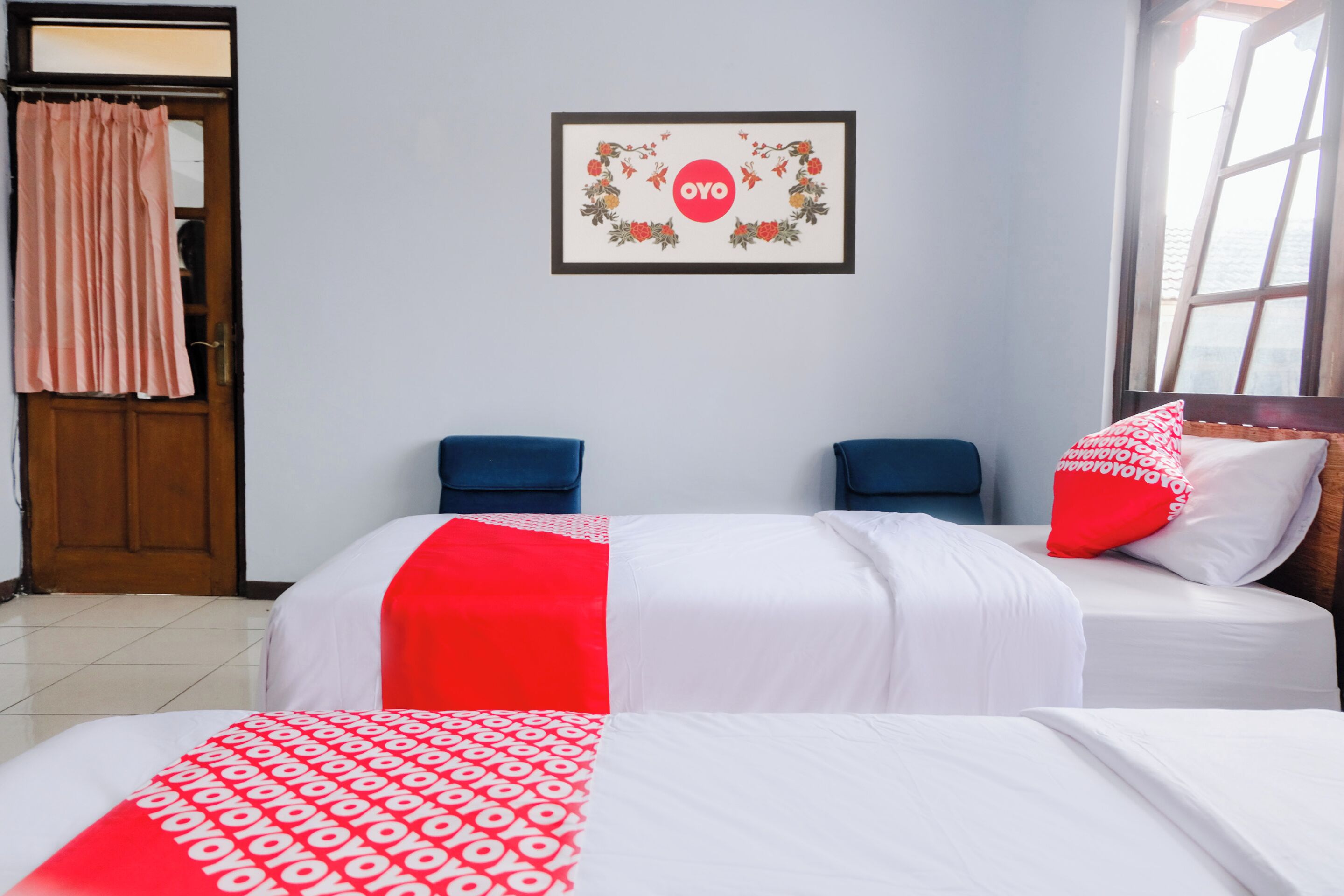 Une chambre d’hôtel avec deux lits, un tableau encadré au mur, une porte avec un rideau et une fenêtre.
