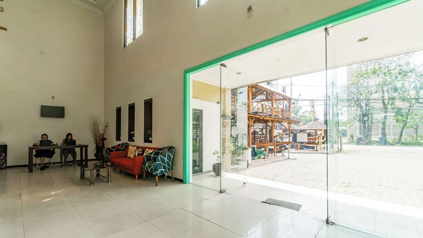 Eine großzügige Lobby mit einer roten Couch, einer Glastrennwand und Blick auf einen Außenbereich mit einer Holzkonstruktion.