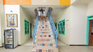 Eine Treppe mit bunten Fliesen und blauen Geländern, die zu einer Zwischenebene führt, auf der die Etage ausgeschildert ist.