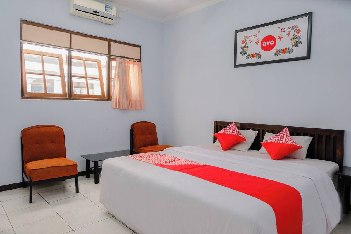 A hotel room with a bed, two chairs, a small table, and a window with curtains.