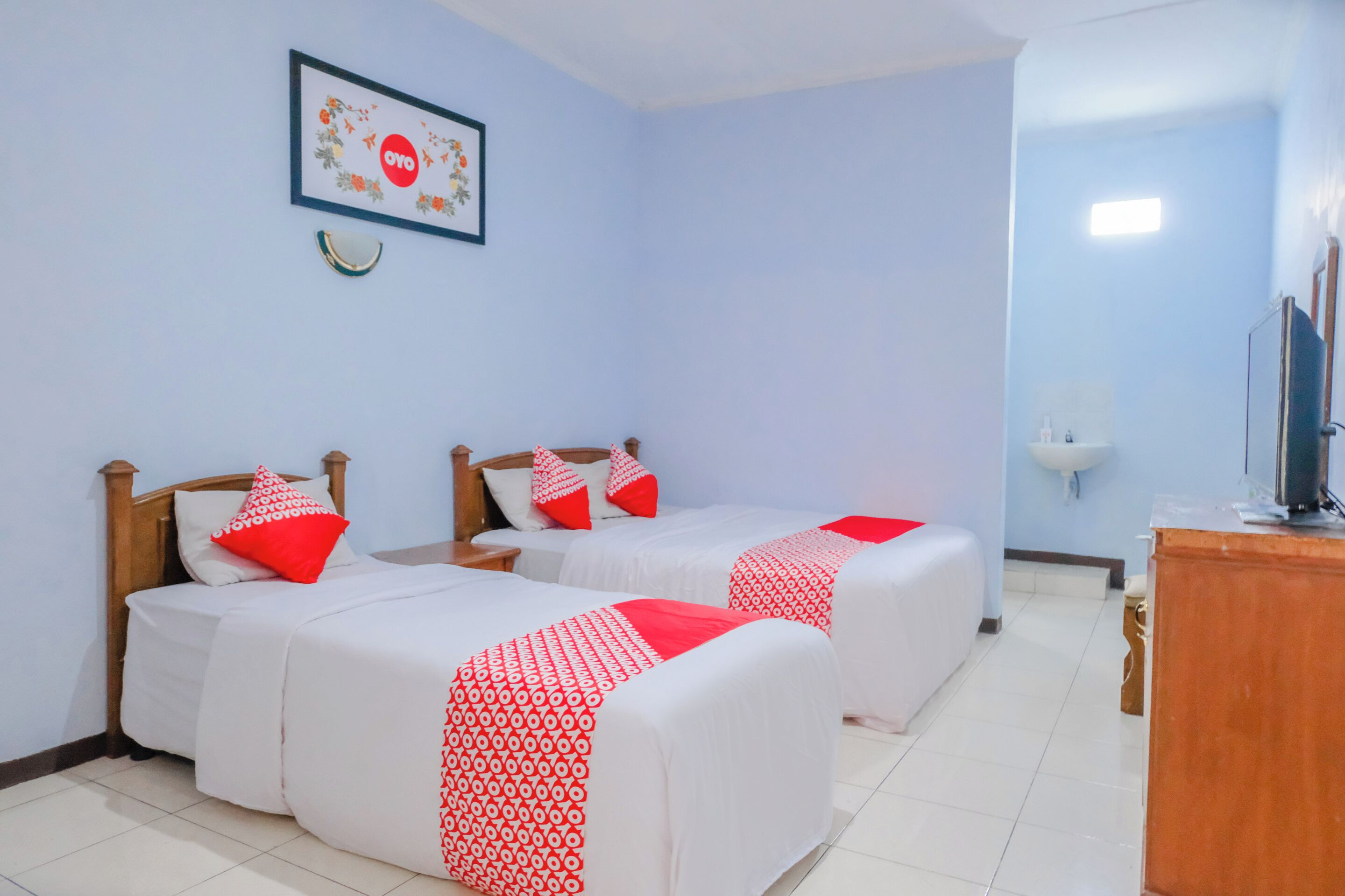 Habitación de hotel con dos camas, cabecera de madera, un escritorio pequeño y un cuadro en la pared.