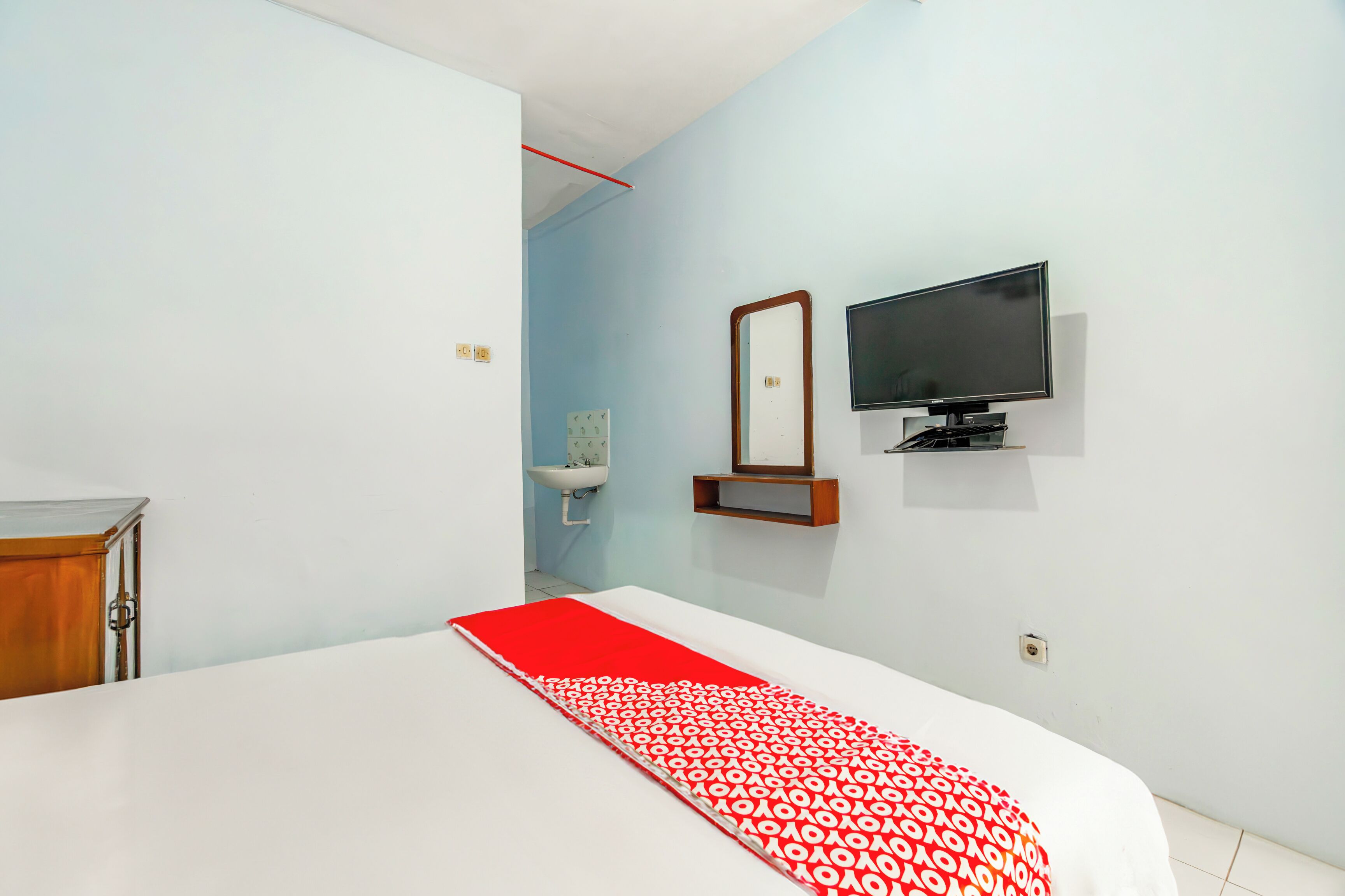 Habitación de hotel con una cama, televisor montado en la pared, una pequeña estantería y ventana con vista al exterior.