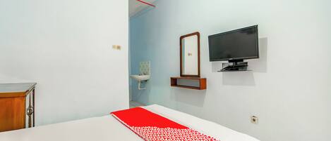 Habitación de hotel con una cama, televisor montado en la pared, una pequeña estantería y ventana con vista al exterior.