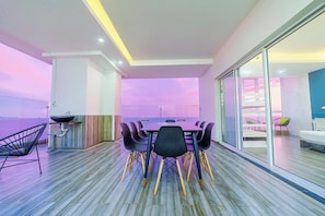 Uma sala de jantar moderna com uma mesa grande e cadeiras, um bar e vista para o mar.