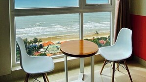 Une pièce dotée d’une grande fenêtre donnant sur l’océan, de deux chaises blanches et d’une petite table ronde.