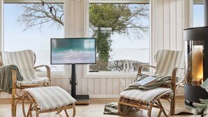 A cozy room with wicker chairs, a flat-screen TV, and a fireplace. - "Titta" - 10m to the fjord by Interhome (Holbæk)