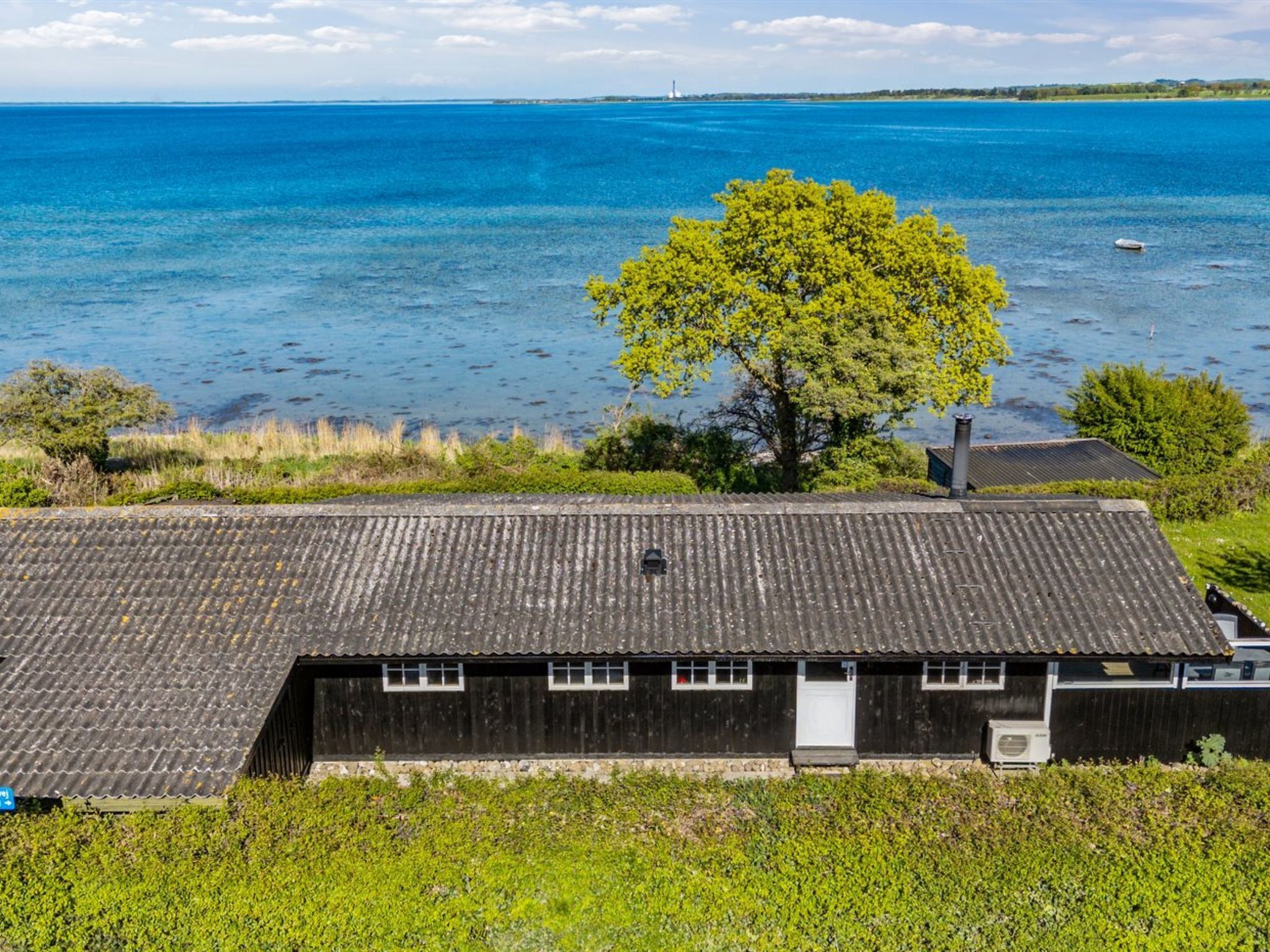 A coastal house with a corrugated metal roof, a small porch, and a view of the sea.