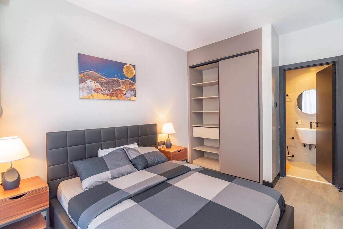 A modern bedroom with a large bed, bedside tables, a wardrobe, and a bathroom visible through an open door.