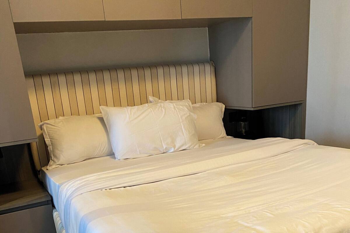 A neatly made bed with a striped headboard, a wooden floor, and a small bedside table.