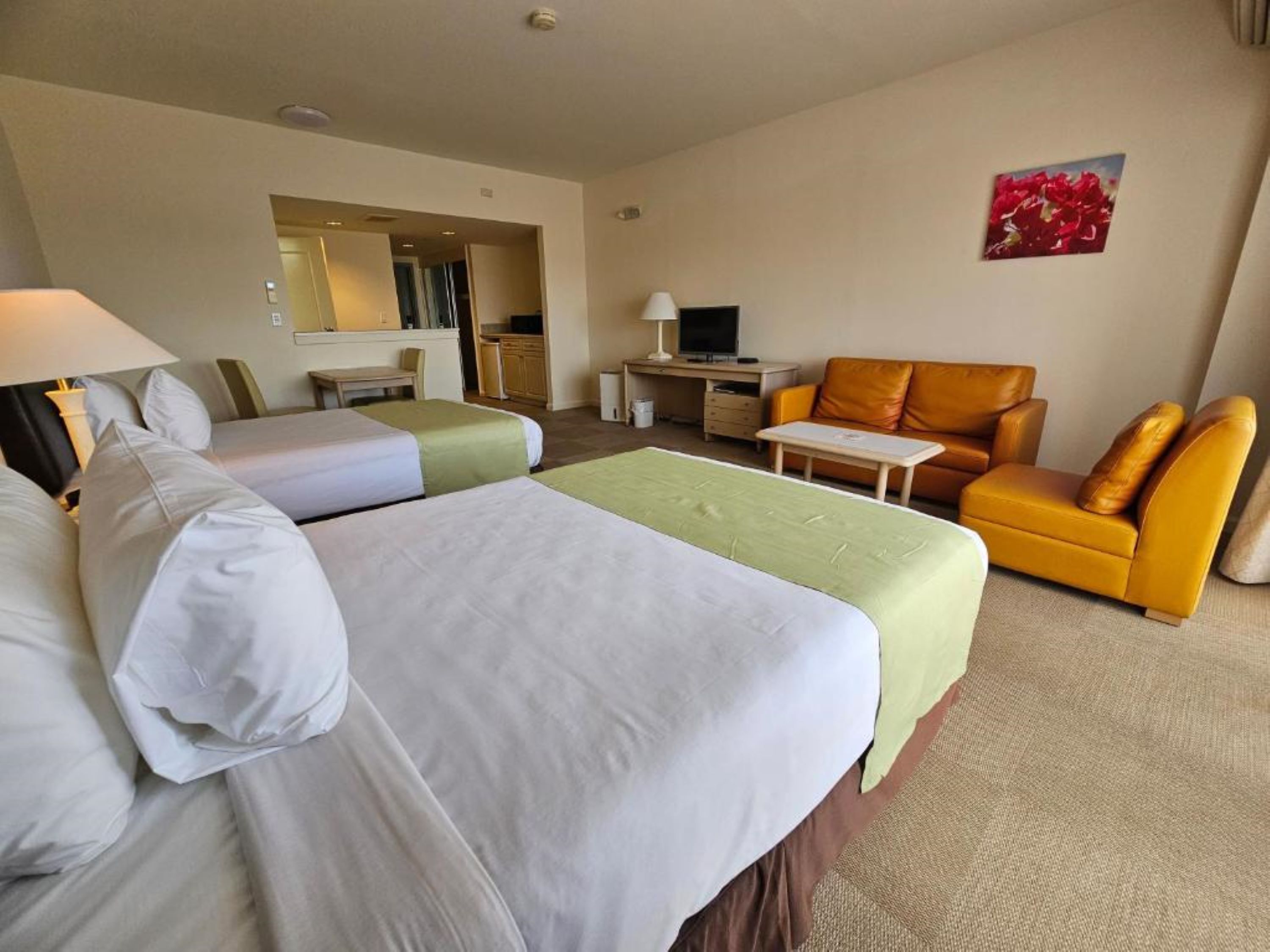 Habitación de hotel con dos camas, un sofá, un escritorio, un televisor y un baño visible a través de una puerta abierta.