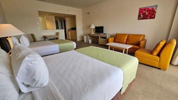 Habitación de hotel con dos camas, un sofá, un escritorio, un televisor y un baño visible a través de una puerta abierta.