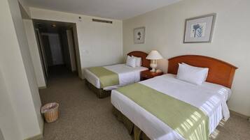 Quarto de hotel com duas camas de solteiro, cabeceira de madeira, abajur, cesto de lixo e um quadro na parede.