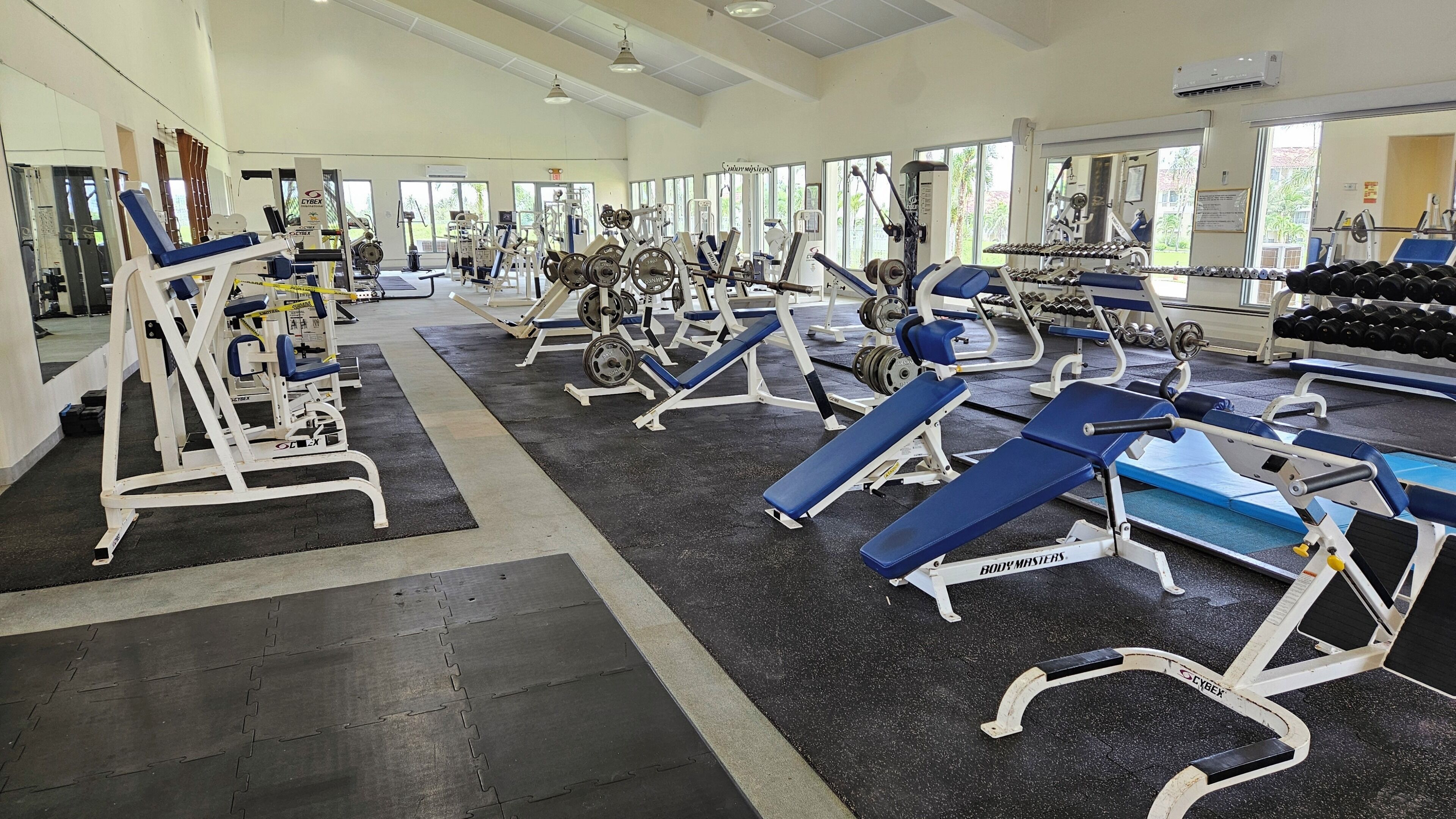 A gym with various exercise equipment, mirrors, and large windows.