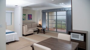 A hotel room with a bed, a sofa, a dining table, a TV, and a balcony with a view.