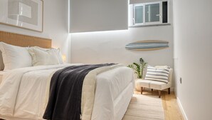A bedroom with a bed, a bedside table, a chair, a window, and a wall-mounted shelf. - Seashell, a Home in Madeira (Machico)