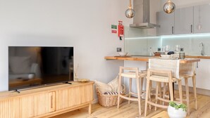 A modern kitchen with a wooden dining table, bar stools, a TV, and a hanging light fixture. - Seashell, a Home in Madeira (Machico)