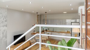 A modern interior with a staircase leading to a second floor, a kitchen area with white cabinets, and a dining space with a table and chairs. - Seashell, a Home in Madeira (Machico)