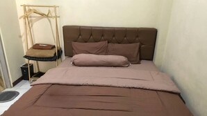 Un letto ben rifatto con una testiera marrone e biancheria da letto coordinata, un comodino con una lampada e un appendiabiti.