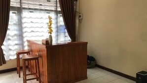 Una stanza con una scrivania in legno e due sgabelli, un vaso con fiori e una finestra con tende.