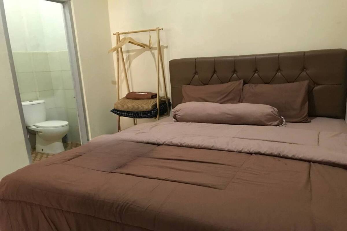Un dormitorio con una cama grande, una silla colgante y un inodoro visible a través de una puerta abierta.