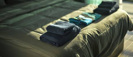 Un lit bien fait, avec des serviettes pliées et une couverture, une fenêtre avec des rideaux et une vue sur la verdure à l’extérieur.