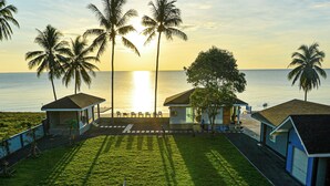 Une vue sur la plage, avec des palmiers, une zone herbeuse et un bâtiment doté d’une porte bleue.