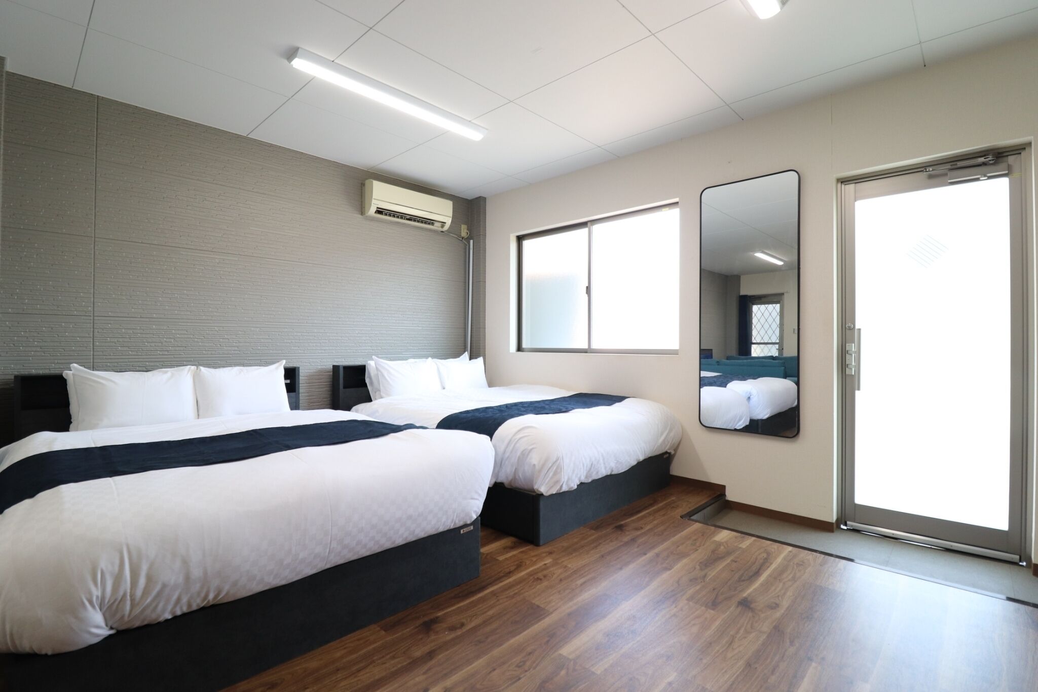 A hotel room with two beds, a large mirror, and a sliding glass door.