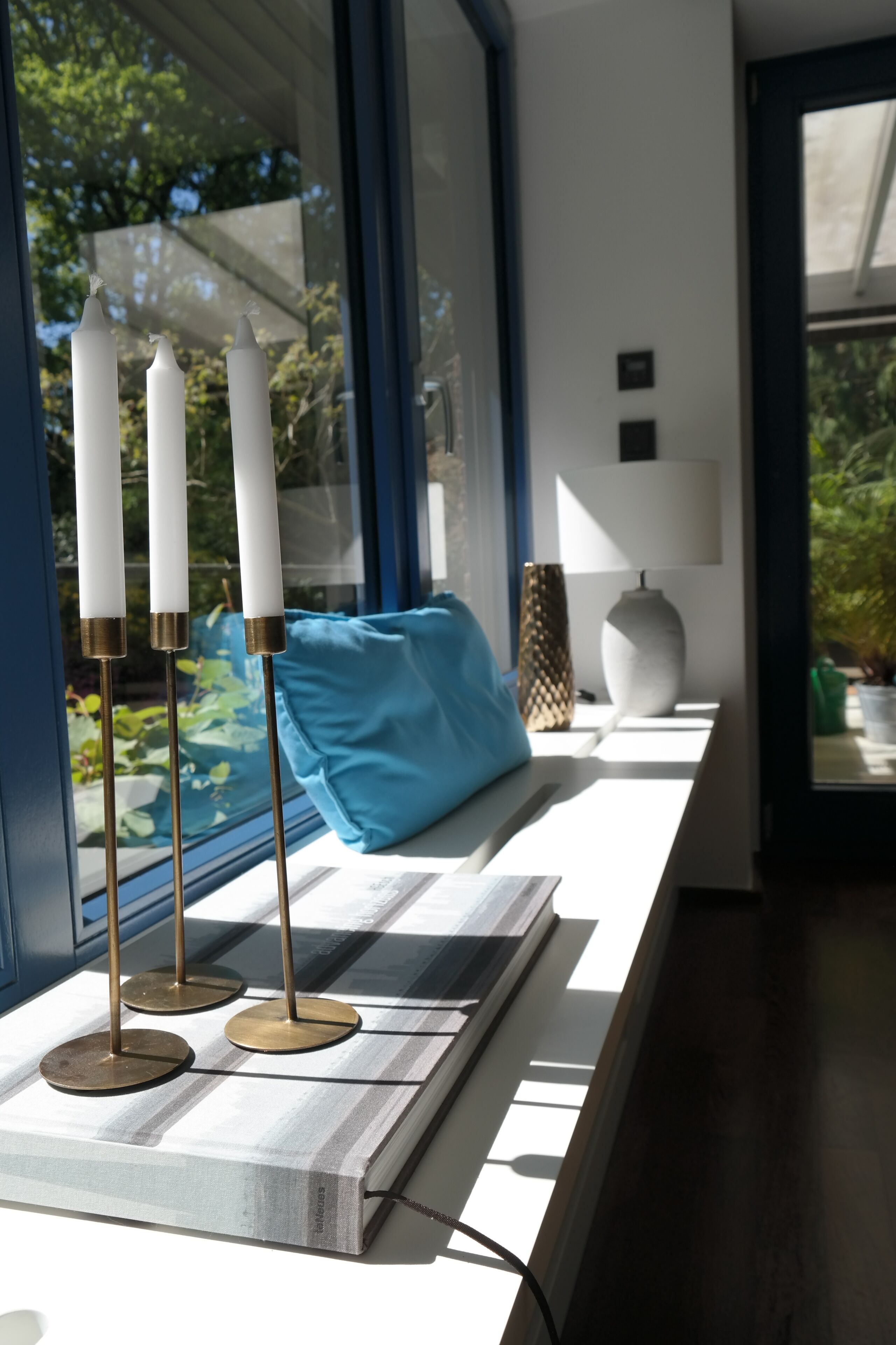 A modern interior with a window sill displaying candles, a blue cushion, and a lamp.