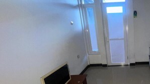 Een gang met een televisie op een bijzettafeltje, een deur met een raam en een lichtschakelaar aan de muur.