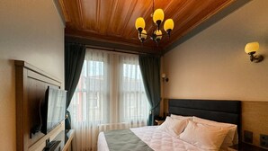 A hotel room with a large bed, a flat-screen TV mounted on the wall, a wooden ceiling, and a window with curtains. - Abelia Mansion Hotel (Istanbul)