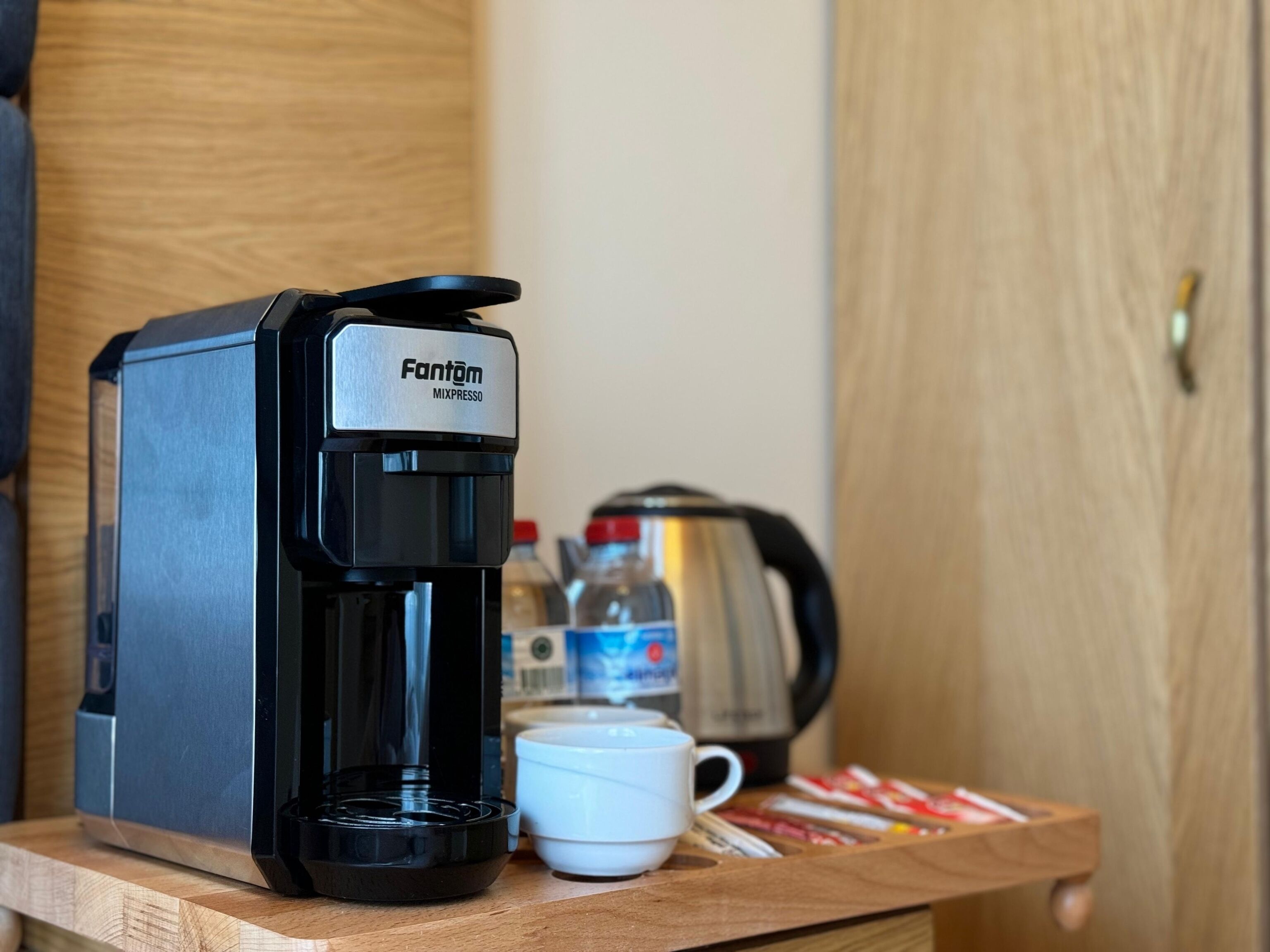 A Fantom Mixresso coffee machine on a wooden table with a white cup and coffee pods nearby.