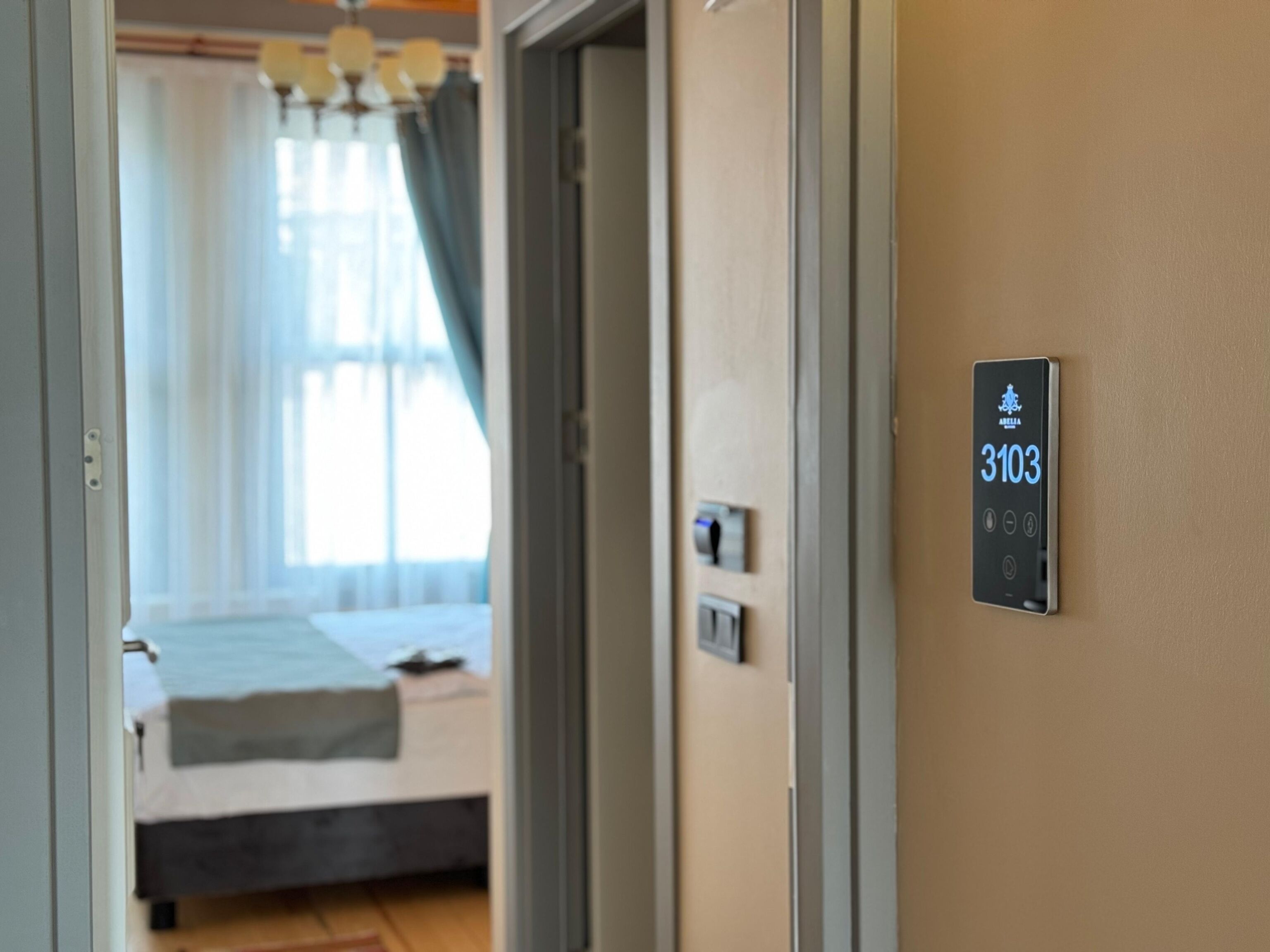 A hotel room with a bed, a bedside table, and a wall-mounted control panel displaying room number 3103.