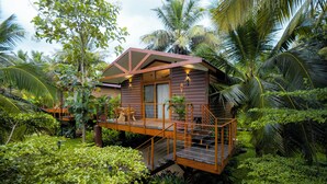 Una casa de madera con balcón, rodeada de abundante vegetación y palmeras.