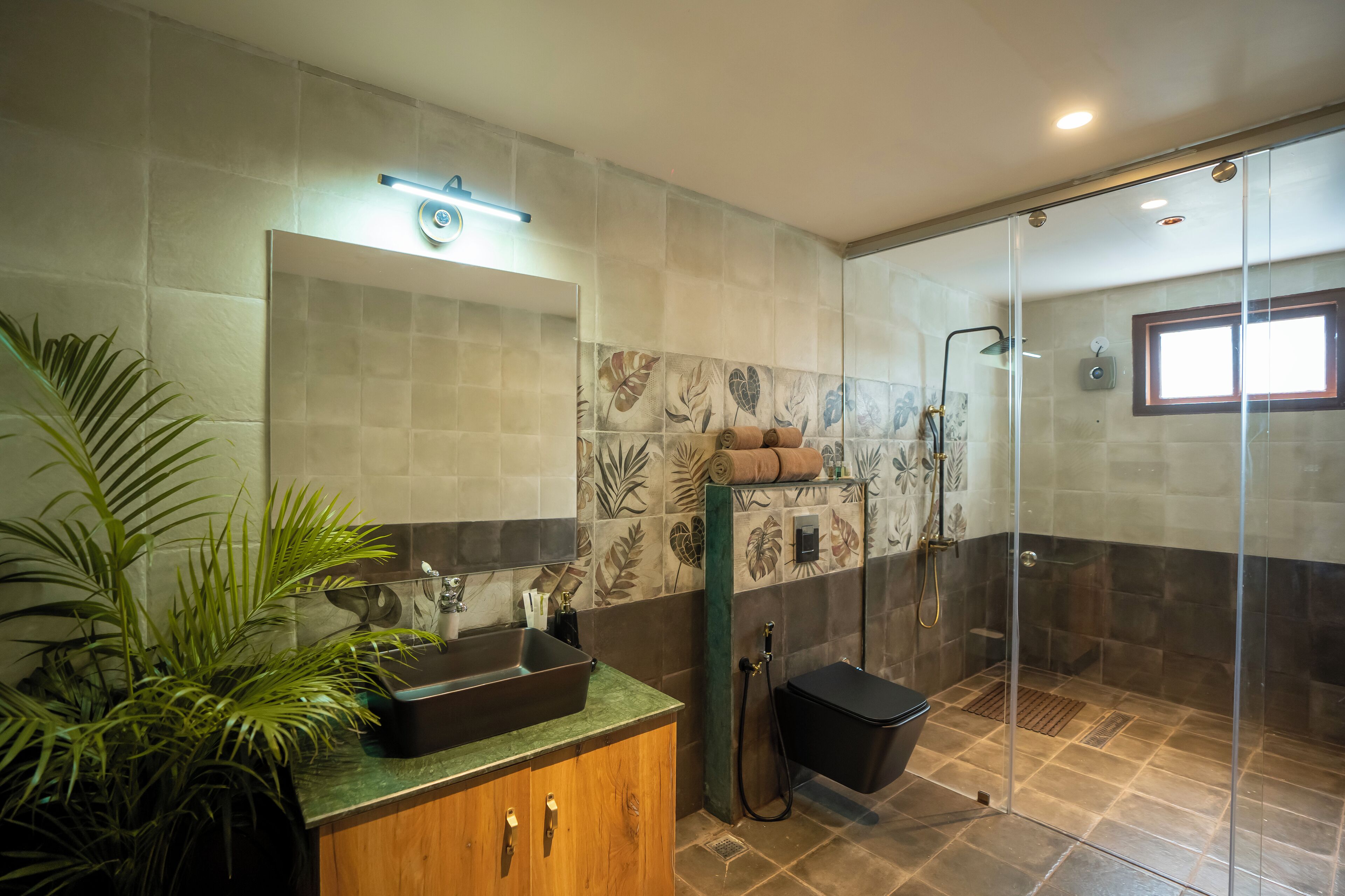 Un bagno moderno con uno specchio grande, un lavabo con piano verde, una doccia con porta in vetro e una pianta in vaso.
