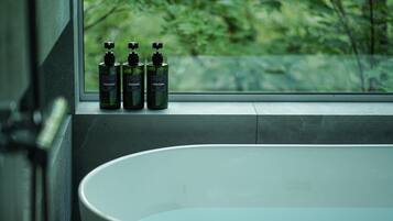 A bathroom with a large bathtub, a window with a view of greenery, and three bottles of shampoo on the windowsill.
