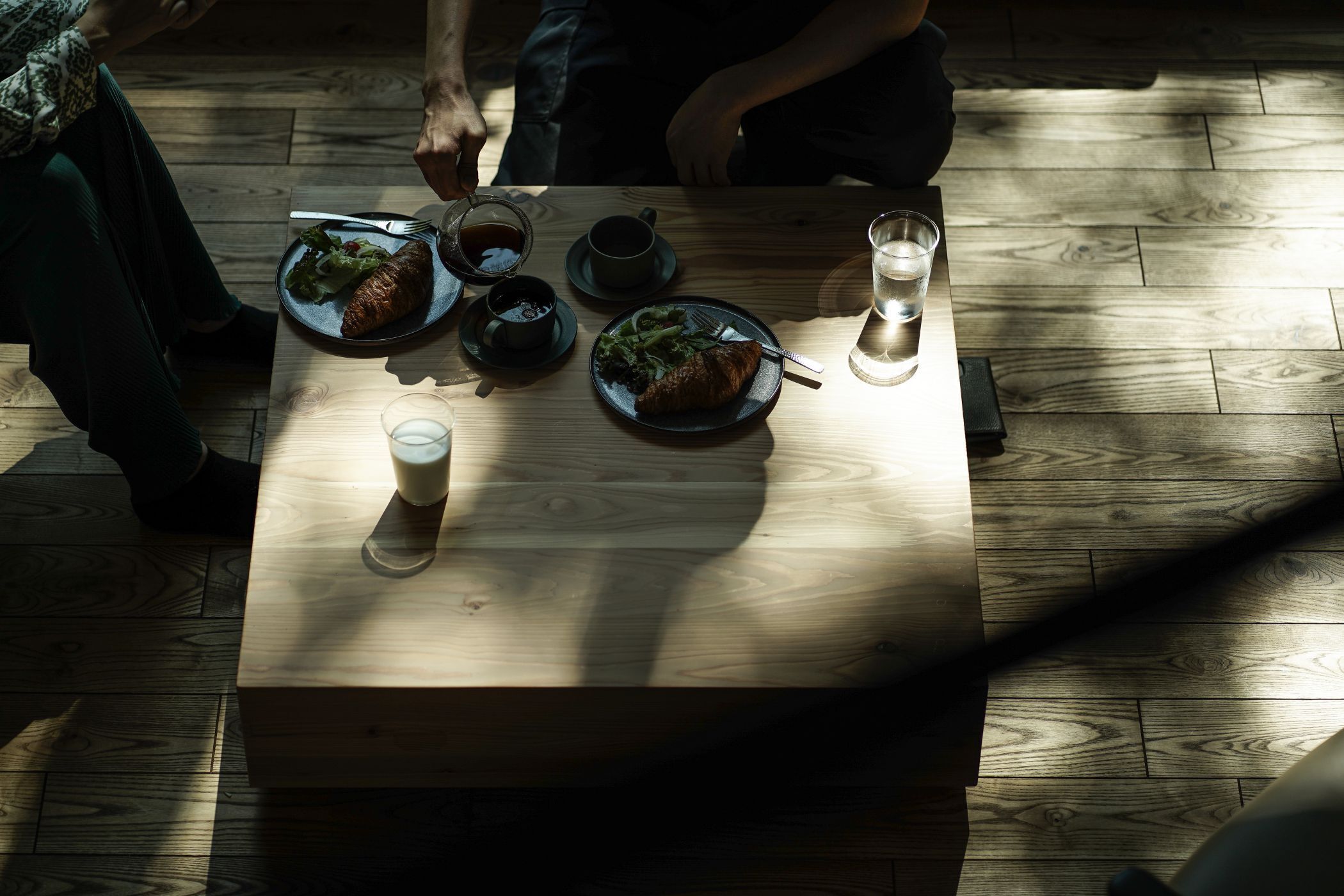 A wooden table with plates of food, cups, and a glass of water.