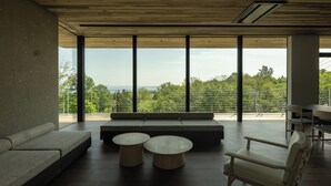 A modern interior with a large window, a sofa, two round tables, and a wooden ceiling. - SANGO (Otaru)