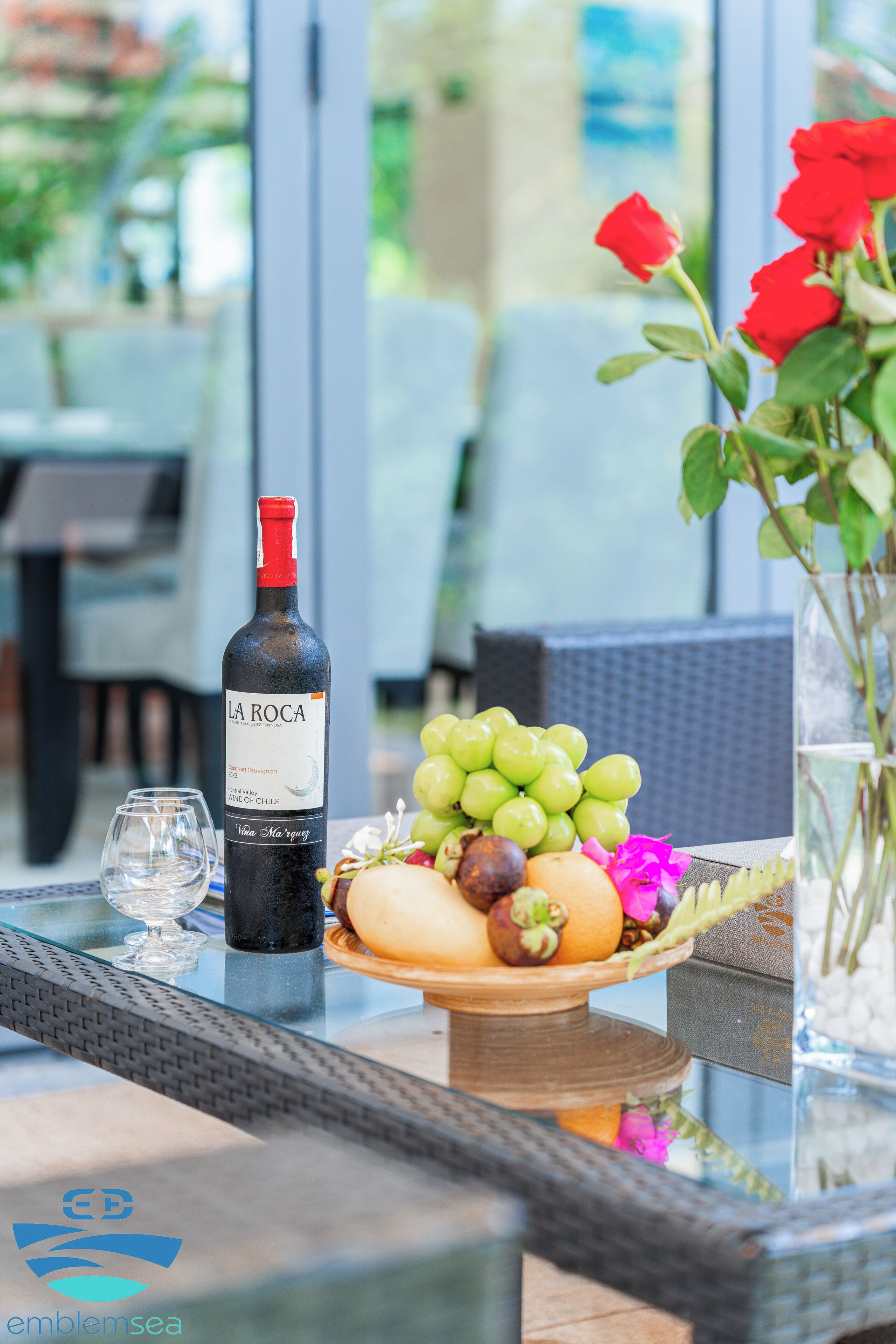 A table with a bottle of La Rocca wine, a bowl of fruit, and a vase with flowers.